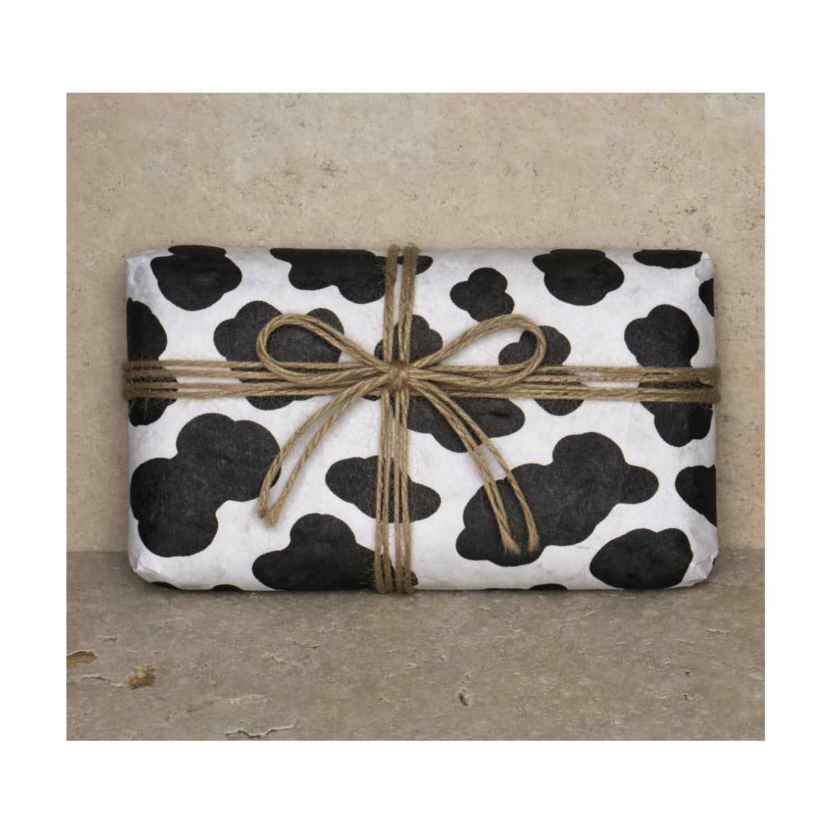 Clay & Colour Gift Wrap - Rectangular package wrapped in black and white cow print paper with a brown string bow on a beige background.